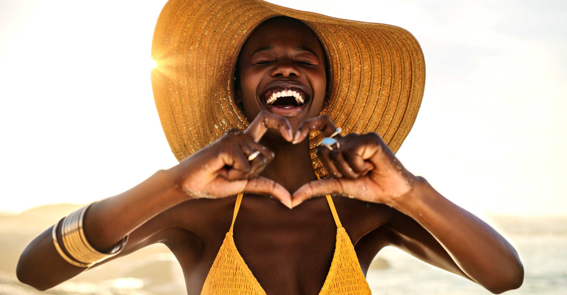 Smiling Black woman in a sunhat making a heart with her hands